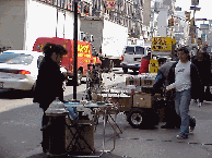 Center right you see vendors selling merchandise on Canal Street.  The woman is making tiny birds from straw that are attached to a mobile or wind chime type decoration.